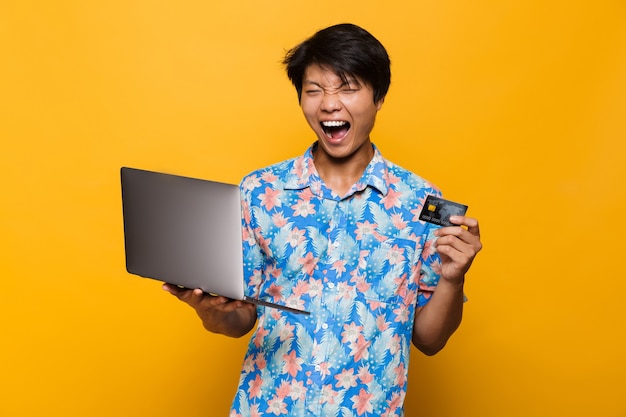 Portrait of a joyful asian man isolated over yellow