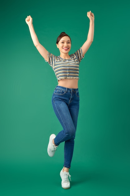 portrait of a joyful attractive Asian girl celebrating success while jumping over green.