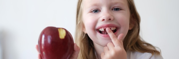 Portrait of joyful child girl without teeth holds apple