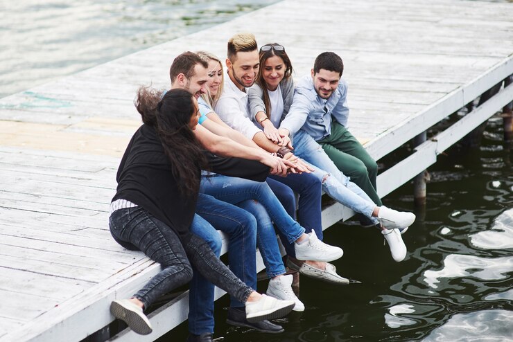 Photo portrait of joyful group of young people sitting on the edge of the pier