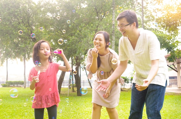 Portrait of joyful happy Asian family playing bubbles together at outdoor park during summer