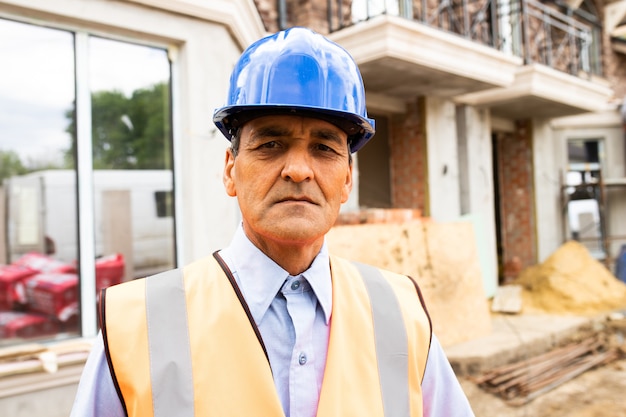 Portrait of joyful indian american man architect at building site looking at camera construction worker wearing blue hardhat and west looking at camera