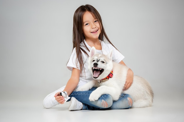 스튜디오 바닥에서 시베리안 허스키 강아지와 즐거운 시간을 보내는 어린 소녀의 초상화. 동물, 우정, 사랑, 애완 동물, 어린 시절, 행복, 개, 라이프 스타일 개념