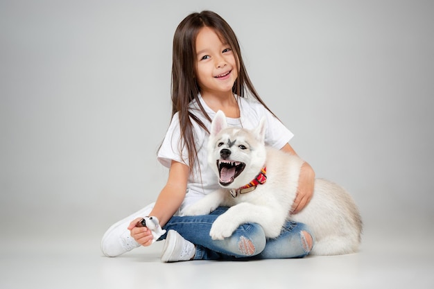 Portrait of a joyful little girl having fun with siberian husky puppy on the floor at studio. the animal, friendship, love, pet, childhood, happiness, dog, lifestyle concept