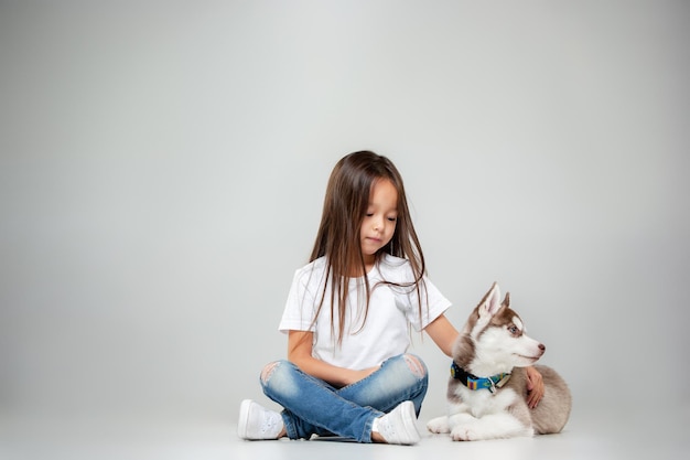 スタジオの床でシベリアンハスキーの子犬を楽しんでいるうれしそうな少女の肖像画。動物、友情、愛、ペット、子供時代、幸福、犬、ライフスタイルの概念