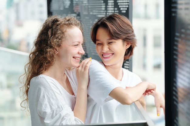 Portrait of joyful pretty young women looking at each other with love and affection when standing on balcony in the morning