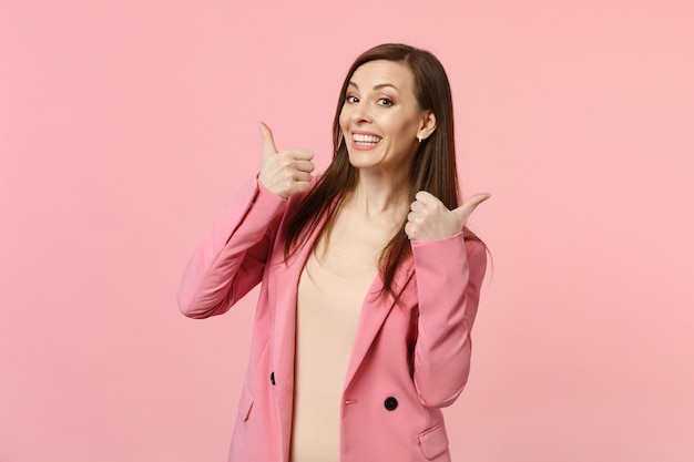 Portrait of joyful smiling young woman wearing jacket looking camera showing thumbs up isolated on pastel pink wall background in studio. People sincere emotions lifestyle concept. Mock up copy space.