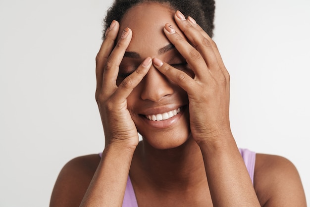 Portrait of joyful woman covering her face and smiling isolated over white wall