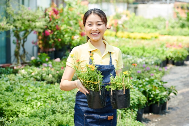 2つの咲く植物でポットを保持しているうれしそうな若いgardeingセンター労働者の肖像画