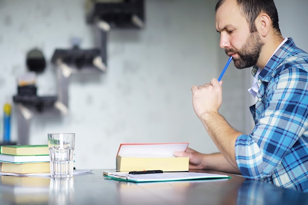 彼のリビングルームの床に座って本を読んでうれしそうな若い男の肖像画。学生が本を持って読んでいます。