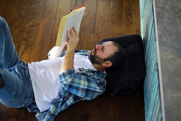 Portrait of joyful young man reading book while sitting on floor in his living roomStudent holding and reading book