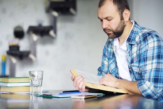 彼のリビングルームの床に座って本を読んでうれしそうな若い男の肖像