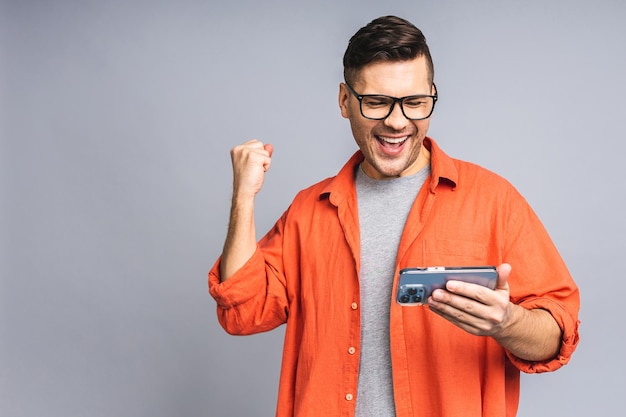 Portrait of a joyful young ukrainian man holding a mobile phone isolated on grey white background celebrating victory Happy winner