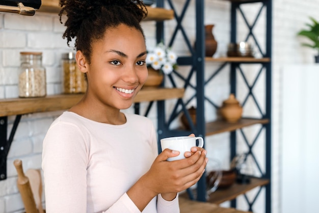 家で一杯のコーヒーを楽しんでいるうれしそうな若い女性の肖像画冬に熱いお茶を飲むかわいい女の子の笑顔居心地の良い日に笑顔の興奮した女性