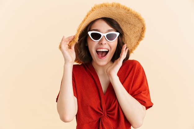 Портрет радостной изумленной отдыхающей женщины в соломенной шляпе и модных солнцезащитных очках радуется изолированно