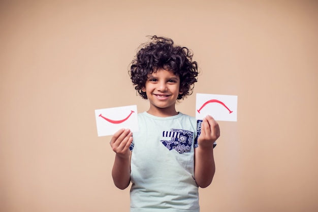 portrait of kid boy holding cards with positive and negative symbol. Children and emotions concept