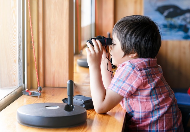 Portrait kid boy looking through of binoculars in the animals station view point.