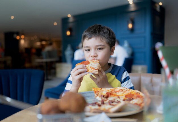 Portrait kid eating home made pizza in the cafe Happy Child boy biting off big slice of fresh made pizza in the restaurant Family happy time concept