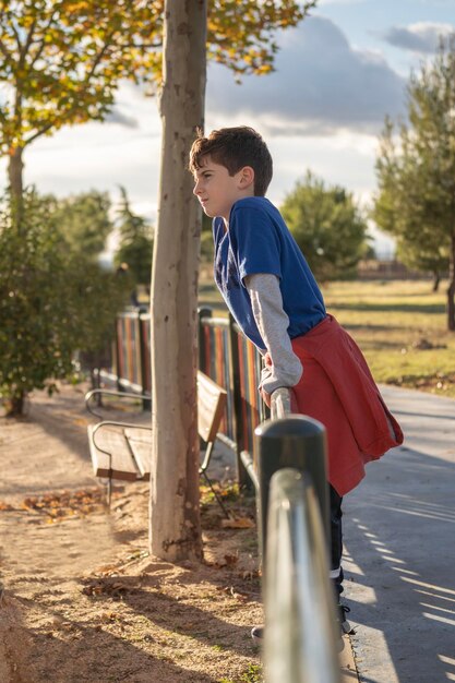 Portrait of a kid looking the playground park from a fence at sunset