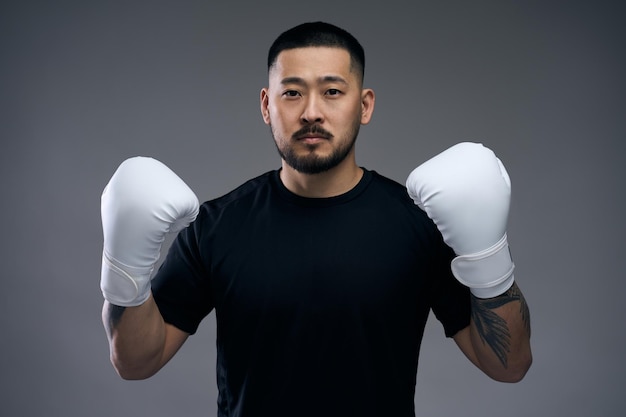 Portrait of korean male boxer in black t shirt wearing white gloves challenging