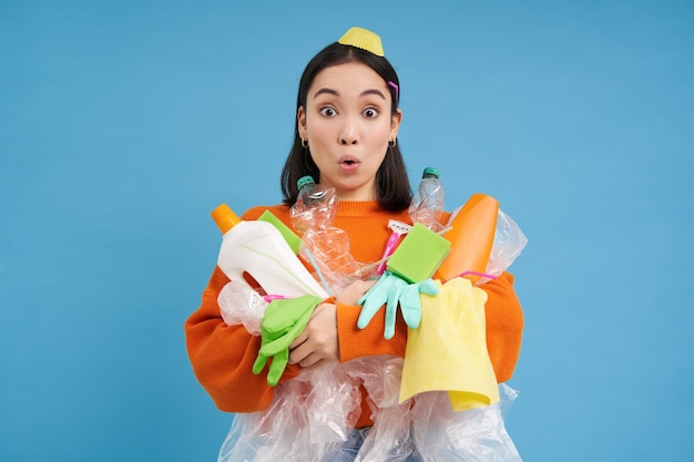 Photo portrait of korean woman with surprised face holding empty plastic bottles and trash for recycling b