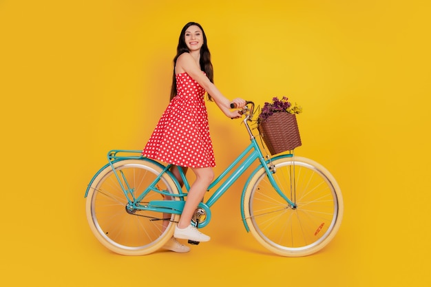 자전거를 타는 여성의 초상화는 노란색 배경에 빨간색 미니 드레스 신발을 신고 여행을 즐깁니다.