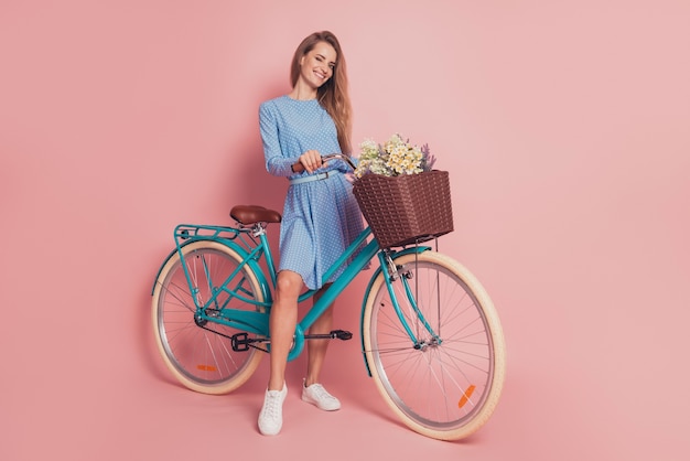 Portrait of lady riding a bike deliver flowers in mini dress shoes on pink background