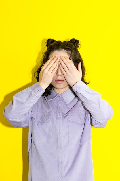 Portrait of a latin woman covering her eyes over yellow background