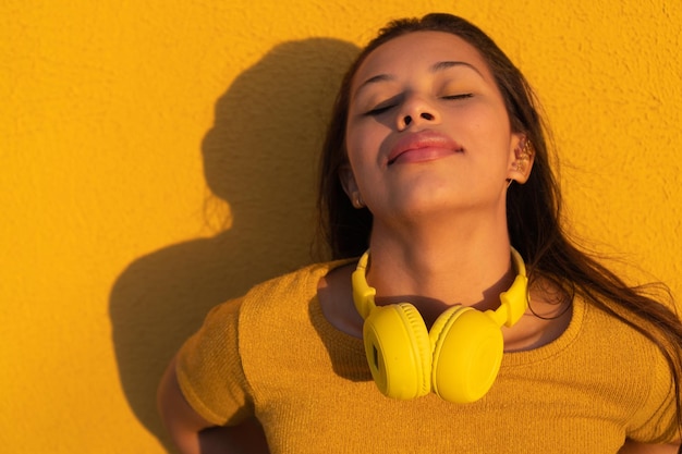 Portrait of a latina woman with yellow musical headphones around her neck yellow tshirt yellow wall background