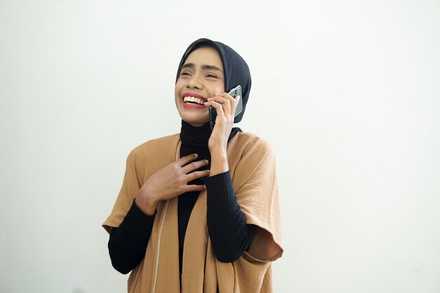 Portrait of a laughing Asian Muslim woman wearing a headscarf making a call with a mobile phone