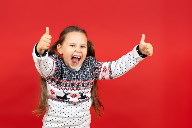 孤立した親指をあきらめるトナカイと白いクリスマスセーターで笑う楽しい女の子の肖像画...