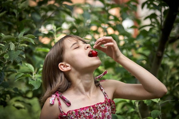 Portrait of laughing little girl eating cherries in the garden