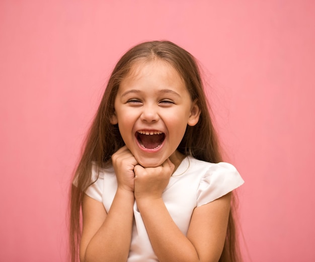 Portrait of a laughing little girl in a white dress on a pink background