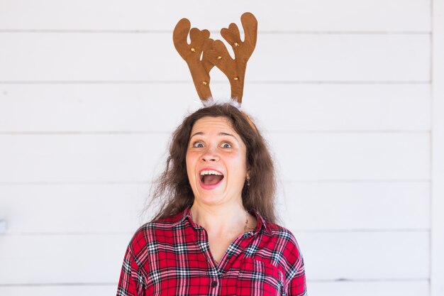 Портрет смеющейся женщины с рогами рождественского оленя на белой стене