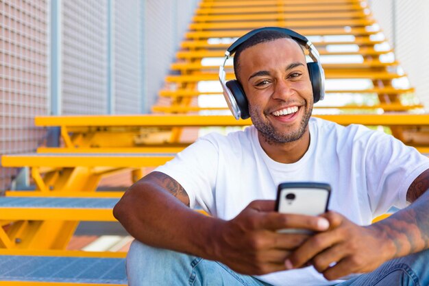 Portrait of laughing young man with headphones and smartphone sitting on stairs