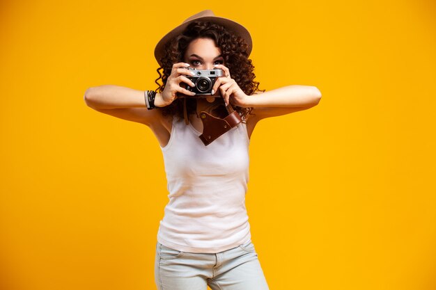 Portrait of laughing young woman taking pictures on retro vintage photo camera isolated on bright yellow