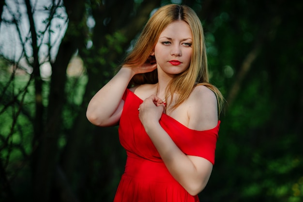 Portrait of light hair girl on red dress in garden.