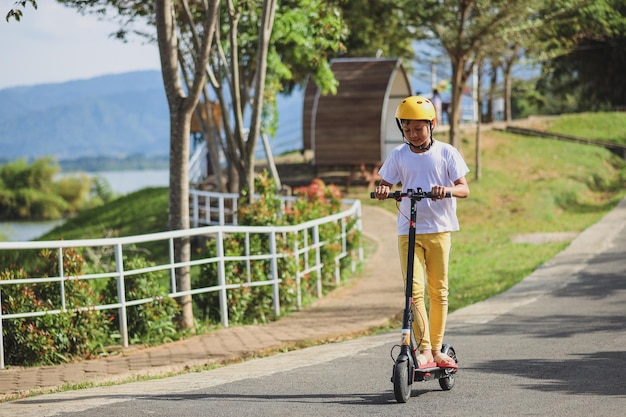 Il ritratto del piccolo ragazzo asiatico indossa il casco divertendosi a cavalcare uno scooter elettrico allo street park ou