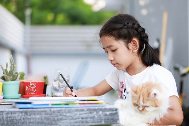 Portrait of a Little Asian girl doing homework and hugging her Persian cat