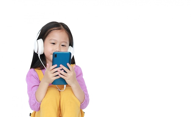 Portrait little Asian girl enjoys listening to music by headphones isolated with copyspace.