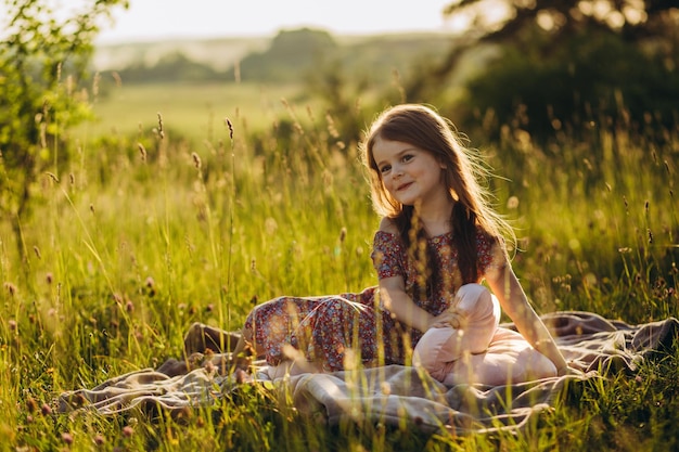 Portrait of Little Baby Girl Sitting on Plaid on Picnic Outdoors at Sunset