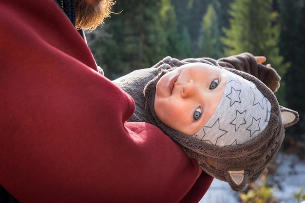 Portrait of little baby traveler in a funny jumpsuit with ears in the arms of a parent