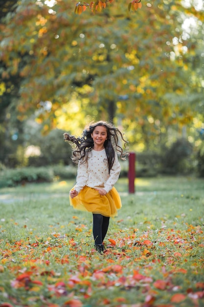 Portrait of a little beautiful girl of 9 years old with long dark hair in bright clothes Happy child in autumn park