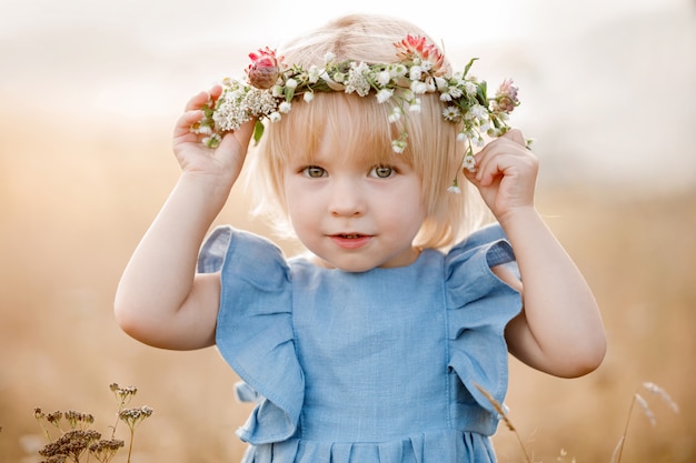 Portrait of a little beautiful girl in floral wreath on nature on summer day