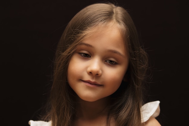 Portrait of a little beautiful girl with long hair against a dark background