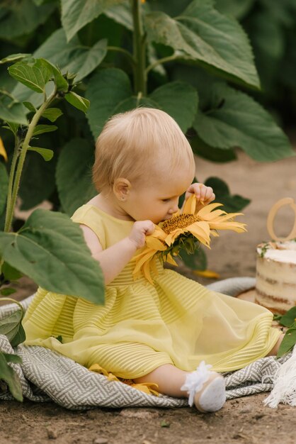 ひまわり畑でケーキと小さな美しい幸せな1歳の女の子の肖像画