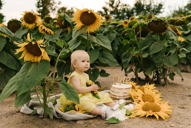 Portrait of a little beautiful happy oneyearold girl with a cake in a field of sunflowers