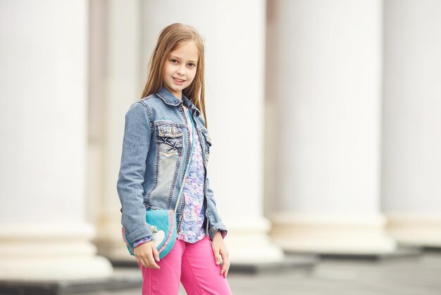 Photo portrait of little beautiful stylish kid girl near columns