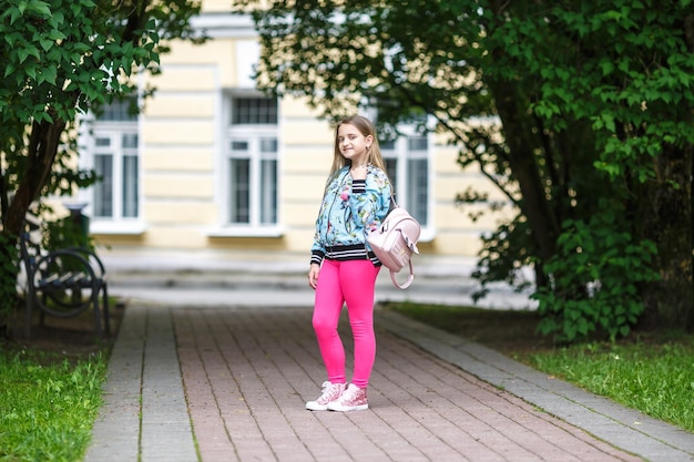 Portrait of little beautiful stylish kid girl with backpack in city park