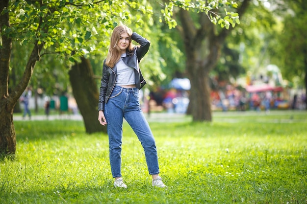 Portrait of little beautiful stylish kid girl with bag in city park on green forest background